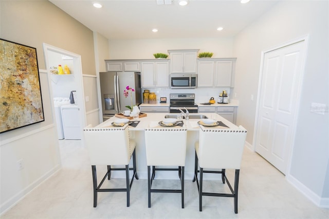 kitchen with appliances with stainless steel finishes, a kitchen island with sink, light countertops, a kitchen bar, and a sink