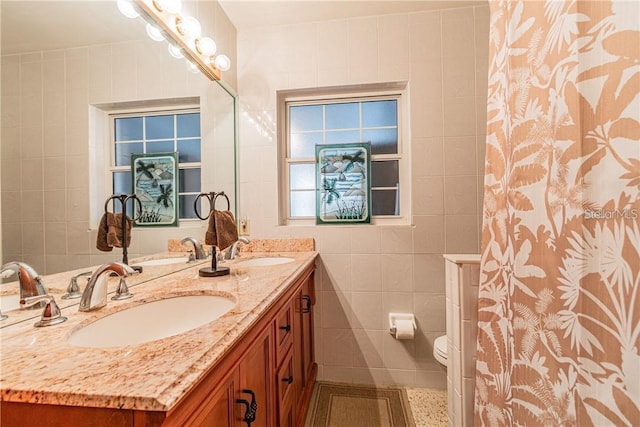 full bathroom featuring toilet, double vanity, a sink, and tile walls