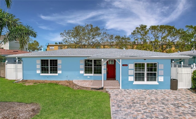 ranch-style home featuring roof with shingles, fence, a front lawn, and stucco siding