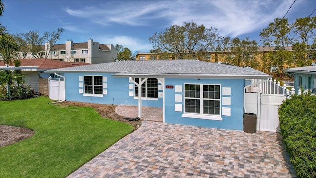 view of front facade featuring roof with shingles, fence, a front lawn, and stucco siding