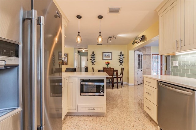 kitchen with light speckled floor, stainless steel appliances, a peninsula, light countertops, and tasteful backsplash