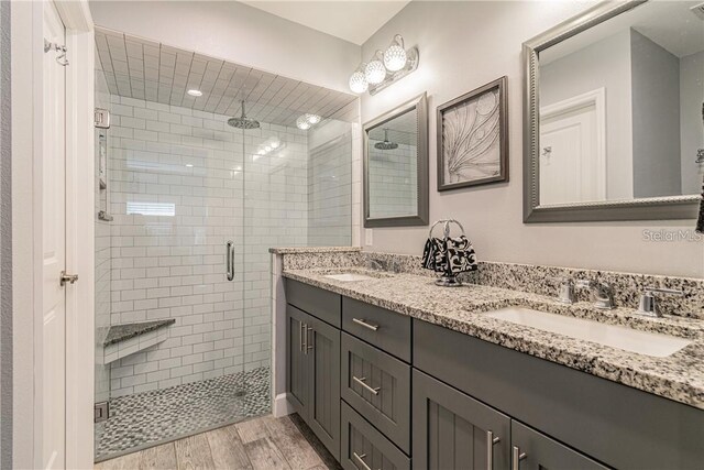 bathroom with double vanity, a sink, a shower stall, and wood finished floors