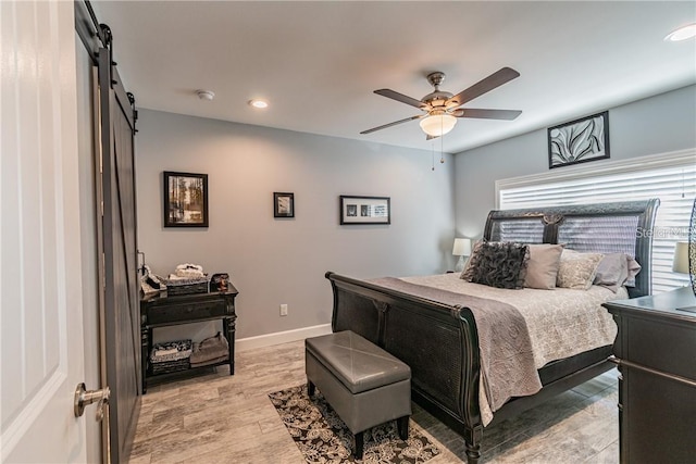 bedroom featuring a barn door, recessed lighting, a ceiling fan, baseboards, and light wood-type flooring