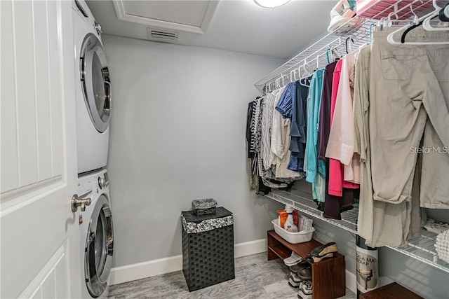 laundry room with laundry area, baseboards, visible vents, stacked washer and clothes dryer, and wood finished floors