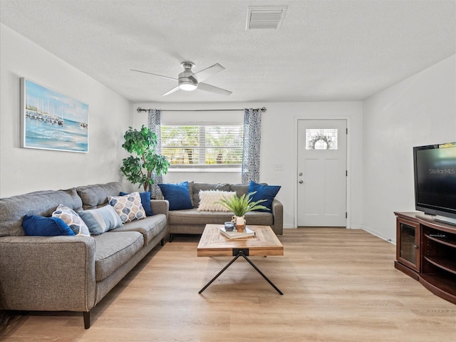 living area featuring a textured ceiling, light wood-style flooring, visible vents, and a ceiling fan