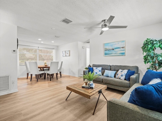 living area with baseboards, visible vents, a textured ceiling, and light wood finished floors