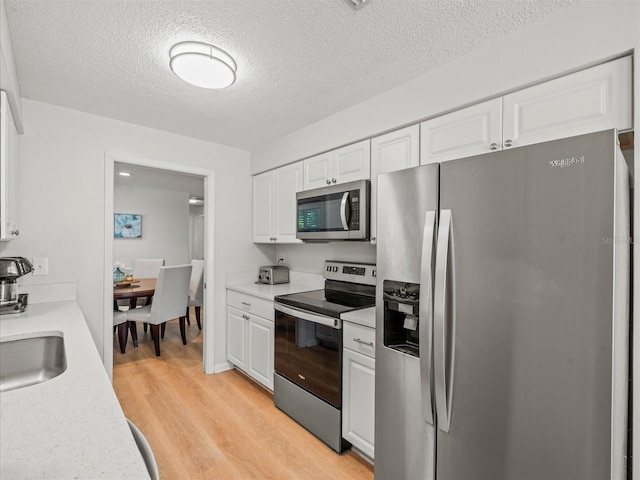 kitchen with stainless steel appliances, a sink, white cabinets, light countertops, and light wood-type flooring