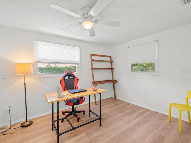 office featuring a textured ceiling, a ceiling fan, light wood-style flooring, and baseboards