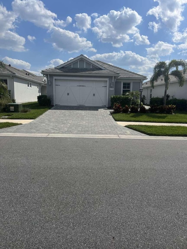 ranch-style home featuring stucco siding, a tile roof, decorative driveway, and a garage