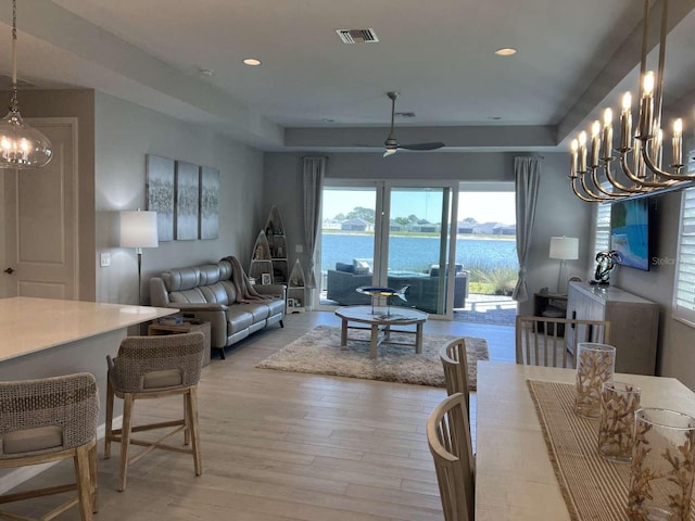 dining room with light wood-type flooring, visible vents, a water view, ceiling fan with notable chandelier, and recessed lighting