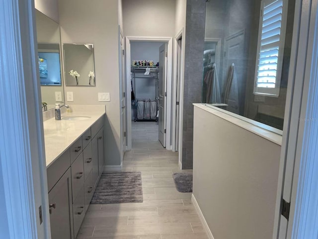 full bathroom with wood tiled floor, vanity, baseboards, walk in shower, and a spacious closet