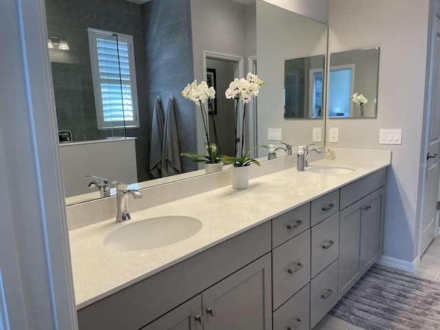 bathroom with double vanity, walk in shower, baseboards, and a sink