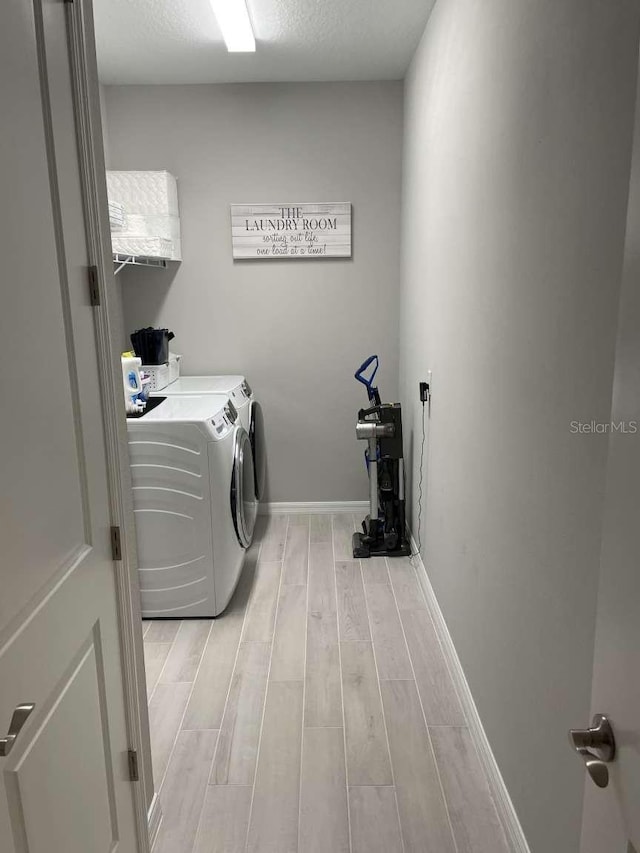 clothes washing area featuring laundry area, wood tiled floor, baseboards, and washer and clothes dryer