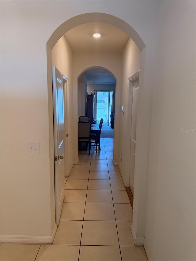 hall featuring light tile patterned floors, arched walkways, and baseboards