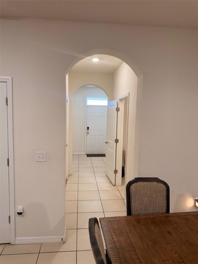 corridor with light tile patterned flooring, baseboards, and arched walkways