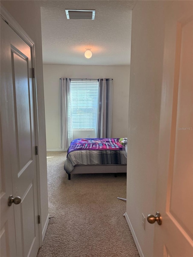 carpeted bedroom featuring visible vents, a textured ceiling, and baseboards