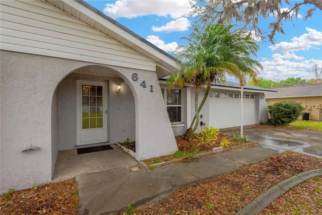 entrance to property with stucco siding, concrete driveway, and a garage