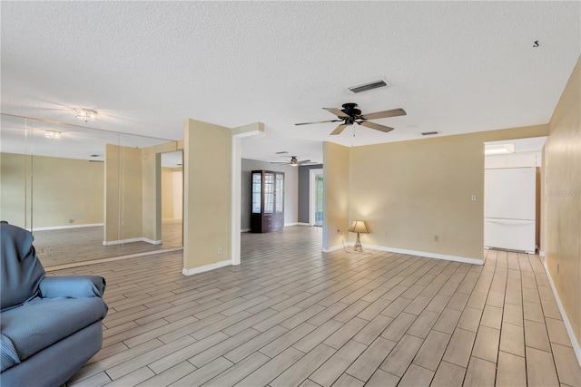 living area featuring baseboards, visible vents, light wood finished floors, and a textured ceiling