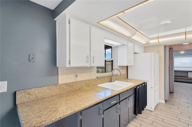 kitchen with a sink, tasteful backsplash, white cabinets, and freestanding refrigerator