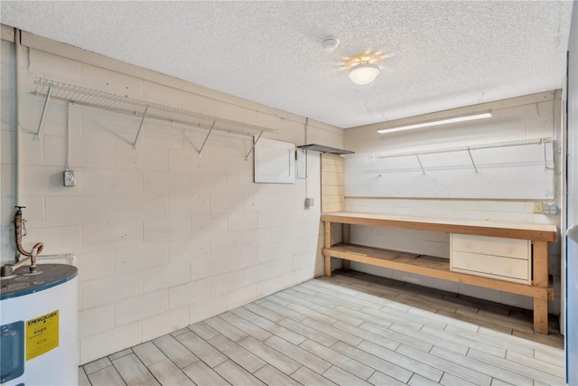 basement featuring water heater, a textured ceiling, concrete block wall, and wood finished floors