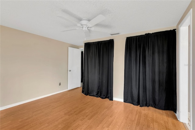 spare room featuring visible vents, a ceiling fan, a textured ceiling, light wood finished floors, and baseboards