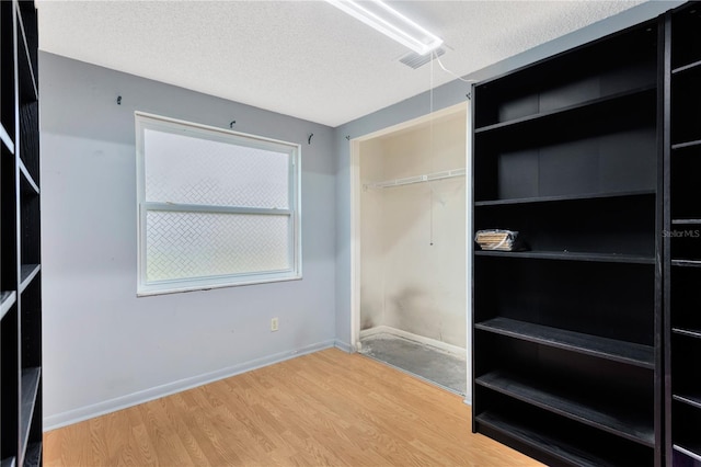 unfurnished bedroom featuring a closet, baseboards, a textured ceiling, and wood finished floors