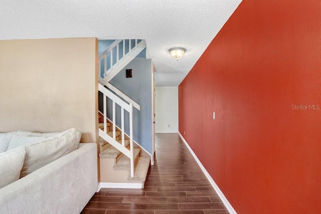 corridor with wood finish floors, a textured ceiling, baseboards, and stairs