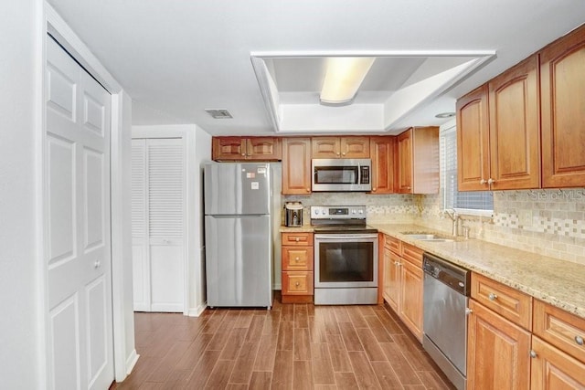 kitchen with light stone counters, a tray ceiling, tasteful backsplash, appliances with stainless steel finishes, and a sink