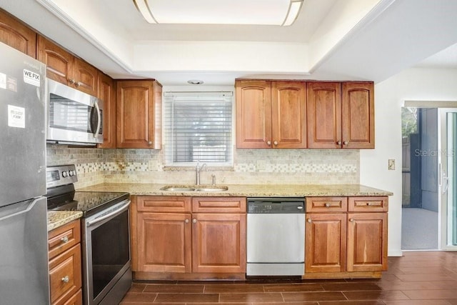 kitchen with appliances with stainless steel finishes, brown cabinets, a sink, and light stone countertops