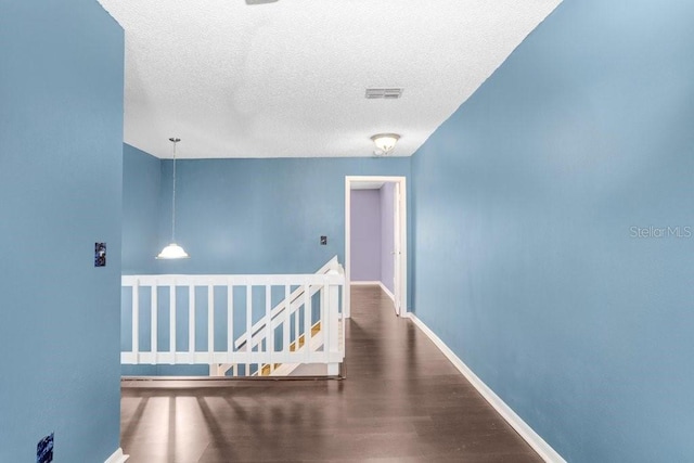 corridor with visible vents, baseboards, wood finished floors, a textured ceiling, and an upstairs landing