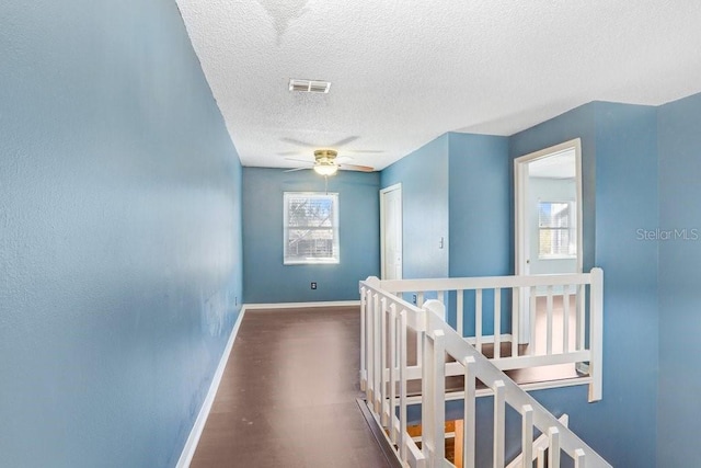 corridor featuring visible vents, a textured ceiling, an upstairs landing, wood finished floors, and baseboards