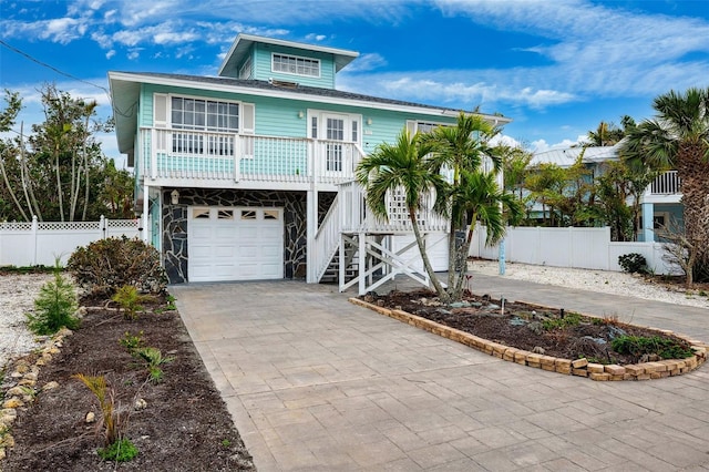 coastal inspired home featuring stairway, fence, driveway, a porch, and an attached garage