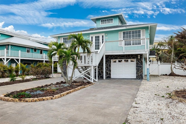 raised beach house featuring a gate, a porch, stairway, concrete driveway, and a garage