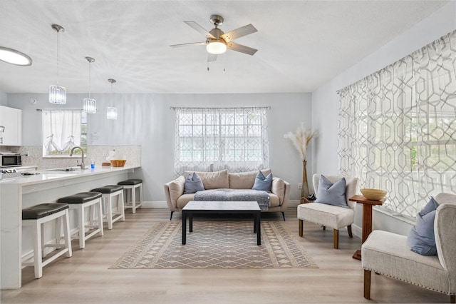 living area featuring a ceiling fan, light wood-style floors, and baseboards