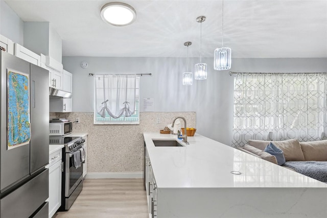 kitchen featuring light wood-style flooring, a sink, white cabinetry, stainless steel appliances, and a peninsula