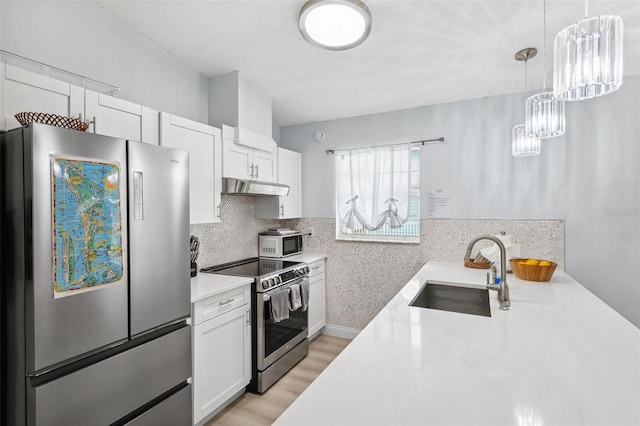 kitchen with light stone counters, a sink, white cabinets, under cabinet range hood, and appliances with stainless steel finishes