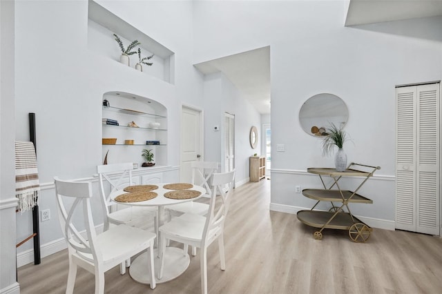 dining room with built in shelves, baseboards, light wood-type flooring, and a towering ceiling