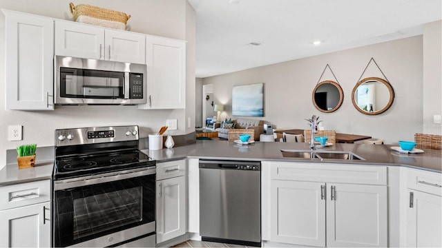 kitchen with a peninsula, appliances with stainless steel finishes, white cabinets, and a sink