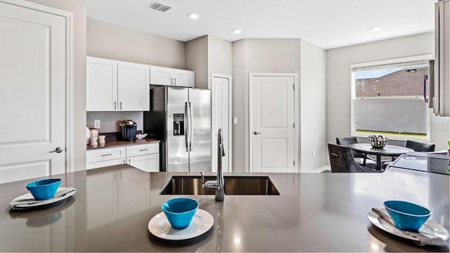 kitchen featuring dark countertops, visible vents, white cabinets, a sink, and stainless steel fridge with ice dispenser