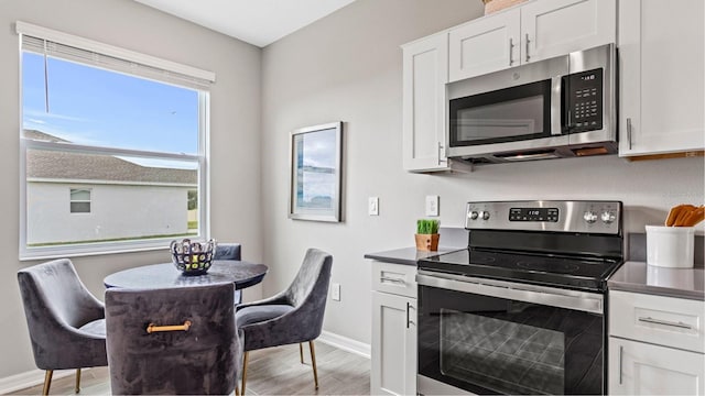 kitchen featuring light wood finished floors, baseboards, dark countertops, appliances with stainless steel finishes, and white cabinetry