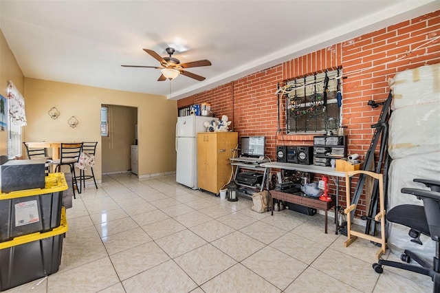 interior space featuring tile patterned floors, brick wall, a ceiling fan, and freestanding refrigerator