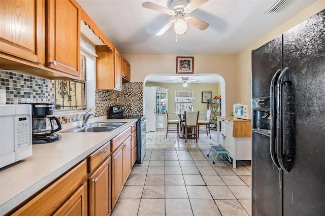 kitchen with electric range, a sink, arched walkways, white microwave, and black refrigerator with ice dispenser