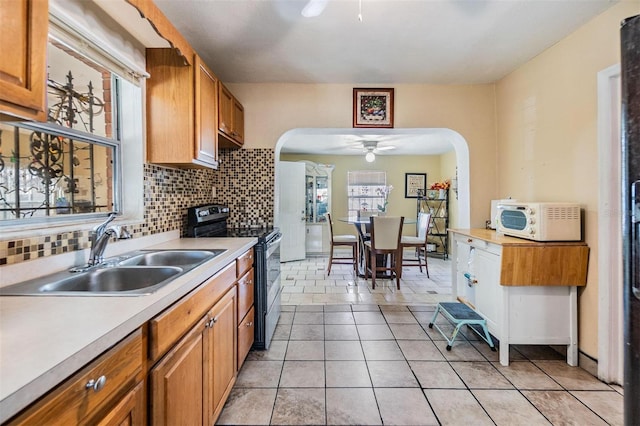 kitchen featuring a sink, arched walkways, stainless steel electric stove, and light countertops