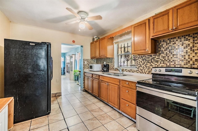 kitchen featuring white microwave, decorative backsplash, stainless steel range with electric stovetop, freestanding refrigerator, and a sink