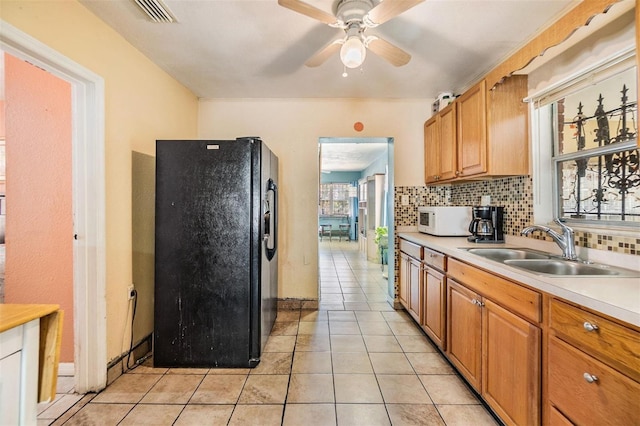 kitchen with a sink, decorative backsplash, white microwave, and black refrigerator with ice dispenser