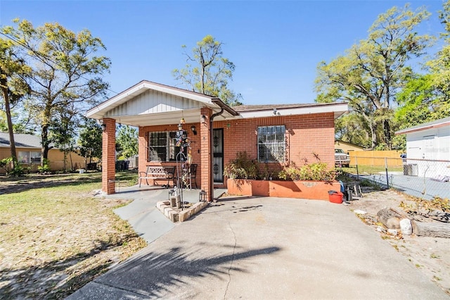 rear view of house featuring brick siding, covered porch, and fence