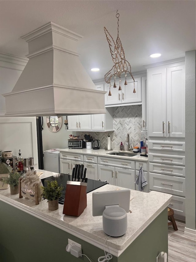 kitchen featuring premium range hood, backsplash, a sink, and white cabinetry