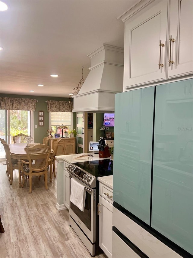 kitchen with light wood finished floors, custom range hood, stainless steel range with electric cooktop, fridge, and white cabinetry