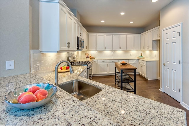 kitchen with stainless steel appliances, a sink, white cabinetry, light stone countertops, and tasteful backsplash