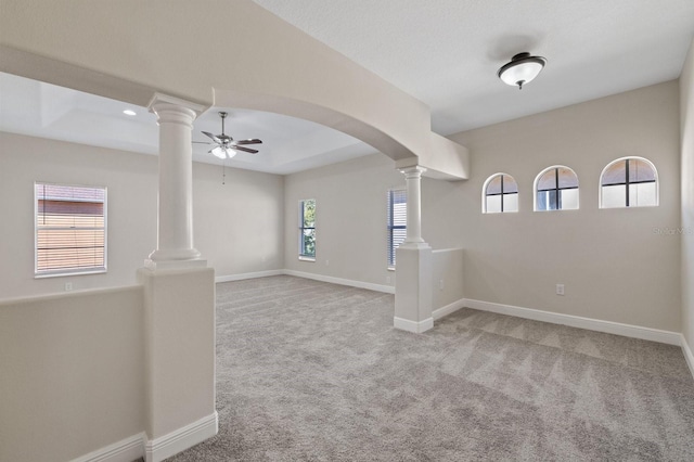 carpeted empty room with arched walkways, baseboards, ceiling fan, and ornate columns